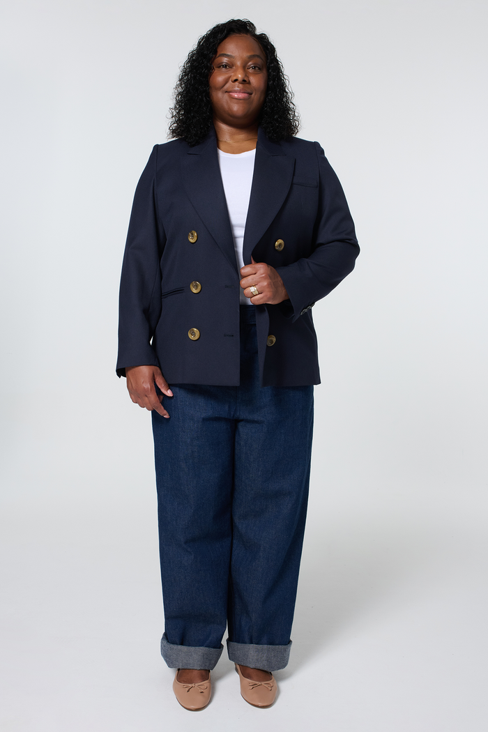 Woman wearing a navy blue blazer, white top, and wide-leg jeans, posing against a white background.