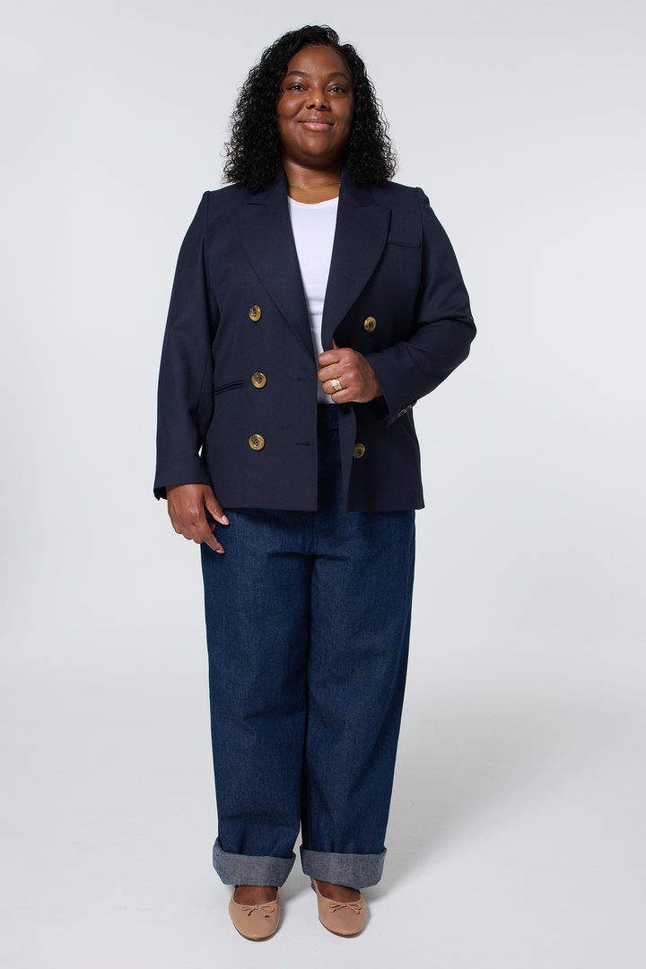 Woman wearing a navy blue blazer, white top, and wide-leg jeans, posing against a white background.