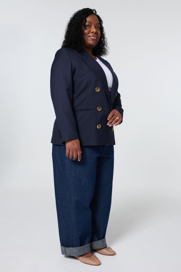 Side view of a woman wearing a navy blue oversized blazer, white top, and wide-leg jeans with cuffs.