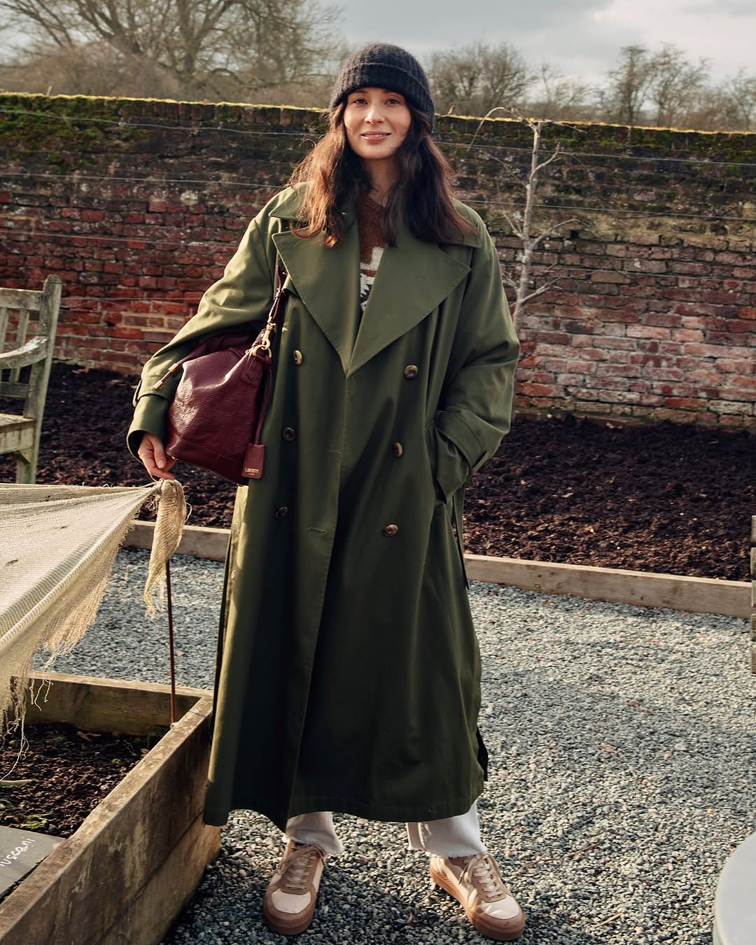 A woman models our sustainable long trench coat in olive green, a versatile and timeless outerwear piece.